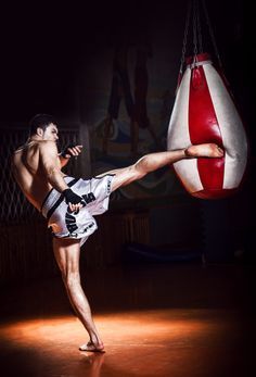 a man kicking a punching bag in the dark with his leg stretched out to kick it