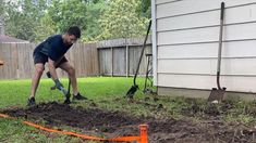 a man is digging in the yard with an orange cone next to him and shovels