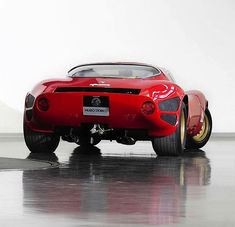 a red sports car sitting on top of a black floor next to a white wall