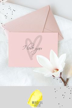 a pink card with the words i love you on it next to a white flower