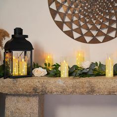 a mantle with candles and flowers on it in front of a circular wall art piece