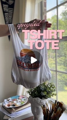 a woman holding up a t - shirt tote in front of a window