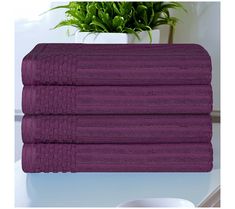 three purple towels stacked on top of each other next to a plant in a white vase