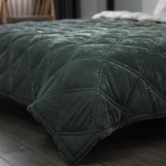 a bed with a green comforter on top of it next to a wooden chair