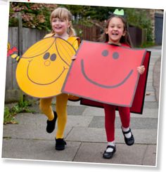 two girls in costumes holding up large pieces of paper with faces on them and smiling