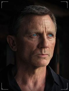 a man with blue eyes stares into the distance while standing in front of a dark background