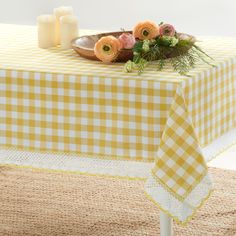 a yellow and white checkered table cloth with flowers on it, next to candles