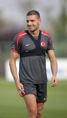 a man standing on top of a soccer field wearing black and red shorts with his hands in his pockets