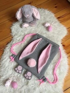 a gray and pink bunny bag sitting on top of a white fluffy rug next to a stuffed animal