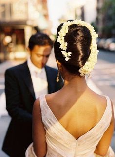 a man and woman standing next to each other in front of a building with flowers in their hair