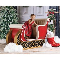 a small child sitting in a sleigh next to a christmas tree