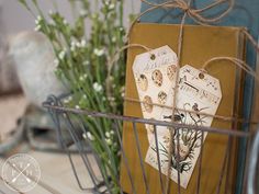 two tags are attached to a wire basket with flowers in the background on a table