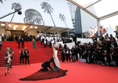 a woman in white dress standing on red carpet next to stairs with photographers taking pictures