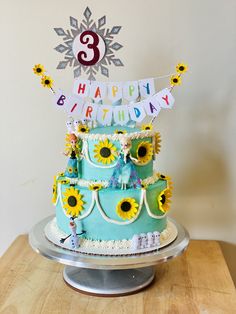 a three tiered birthday cake with sunflowers and decorations on the top layer