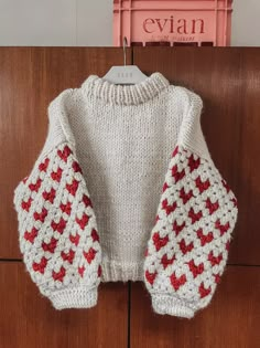 a white sweater with red stars on it hanging from a clothes hanger in front of a wooden door