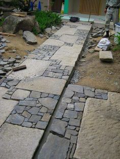 a man standing next to a stone path in the middle of a yard with rocks on it