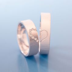 two wedding rings with hearts on them sitting next to each other in front of a blue background