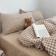 a teddy bear sitting on top of a bed next to pillows and a book laying on it