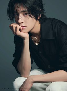 a young man sitting on top of a white chair wearing a black shirt and gold necklace