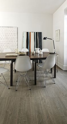 a dining room table with white chairs and art on the wall in the back ground