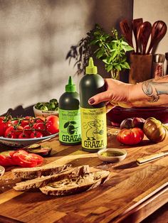 a person holding a bottle of tattoo ink on top of a cutting board next to tomatoes and bread