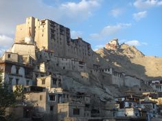 an old building on the side of a hill with buildings below it and mountains in the background