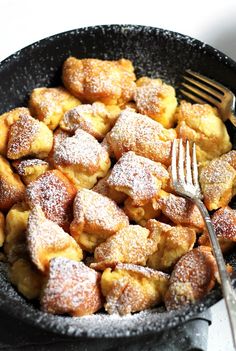 powdered sugar covered pastries in a black bowl with a fork