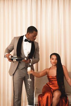 a man in a tuxedo pouring champagne into a woman's hand while sitting on a couch