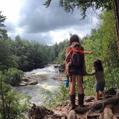 a woman and child are standing on the edge of a cliff overlooking a river with rapids