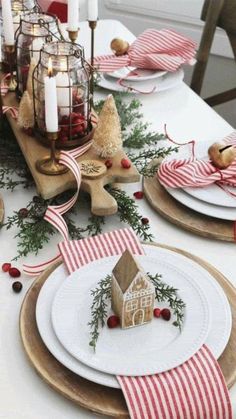 the table is set for christmas dinner with plates and napkins on it, including a gingerbread house