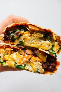 a hand holding two burritos filled with meat and veggies on top of each other