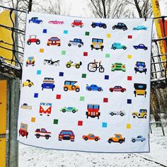 a white quilt with cars and trucks on it hanging from a clothesline in the snow