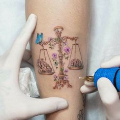 a tattoo artist working on a woman's leg with the scale of justice and flowers