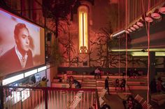 people are sitting on benches in front of a large screen with an image of a man