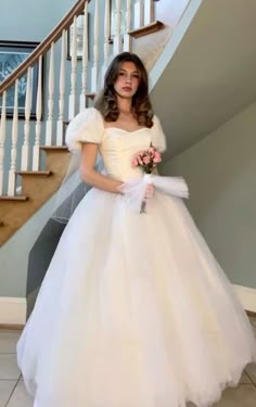 a woman in a white dress standing next to a stair case and holding a bouquet