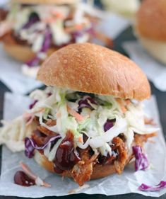 two pulled pork sandwiches with coleslaw and slaw on top, sitting on wax paper