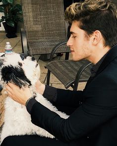 a man sitting on a chair petting a small white and black dog in his lap