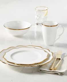 white and gold dinnerware set on a marble table with two glasses, one empty