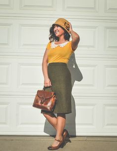 a woman in a yellow shirt and green skirt is holding a brown purse while standing next to a garage door