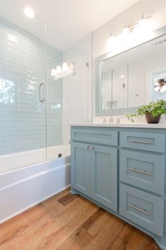 a bathroom with blue cabinets and a white bathtub next to a wooden flooring