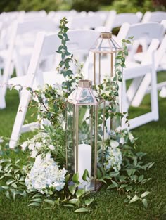 an arrangement of white flowers and candles on the grass at a wedding ceremony with chairs in the background