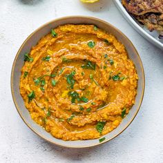 a bowl filled with carrot hummus next to other food on a white counter top