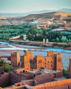 an old castle sits on the edge of a river in front of a small town