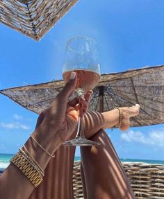 a person holding up a wine glass in front of some umbrellas on the beach