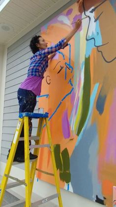 a man is painting on the side of a building with yellow ladders and paint