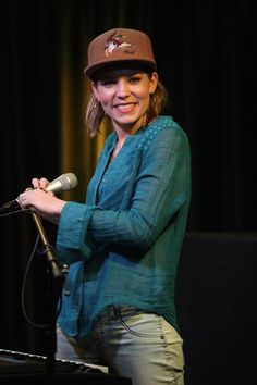 a woman standing in front of a microphone with a hat on her head and smiling at the camera