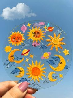 a hand holding up a glass plate with sun and moon designs on the outside, in front of a blue sky