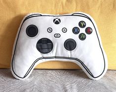 a white controller pillow sitting on top of a bed next to a yellow pillow with black buttons