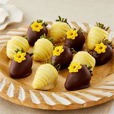 chocolate covered strawberries are arranged on a wooden platter with white and yellow flowers