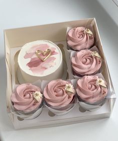 cupcakes with pink frosting and gold decorations in a box on a table